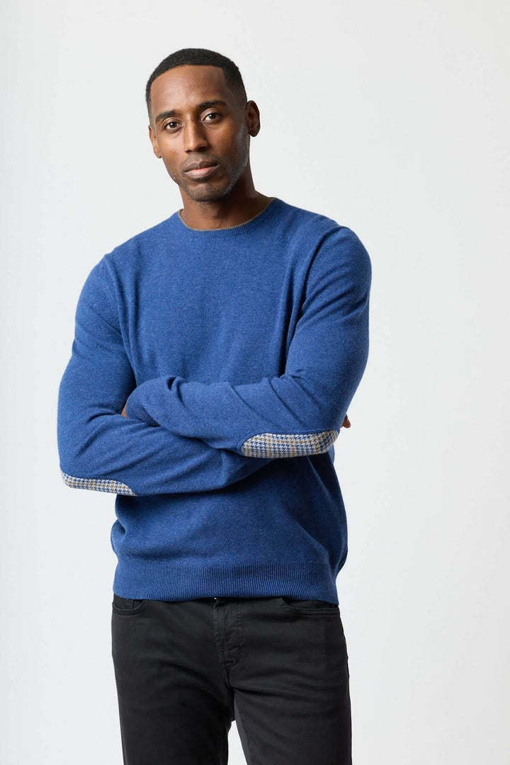 Homme portant un chandail en laine vierge et cachemire bleu avec coudières motif pied-de-poule, élégance italienne et confort absolu.