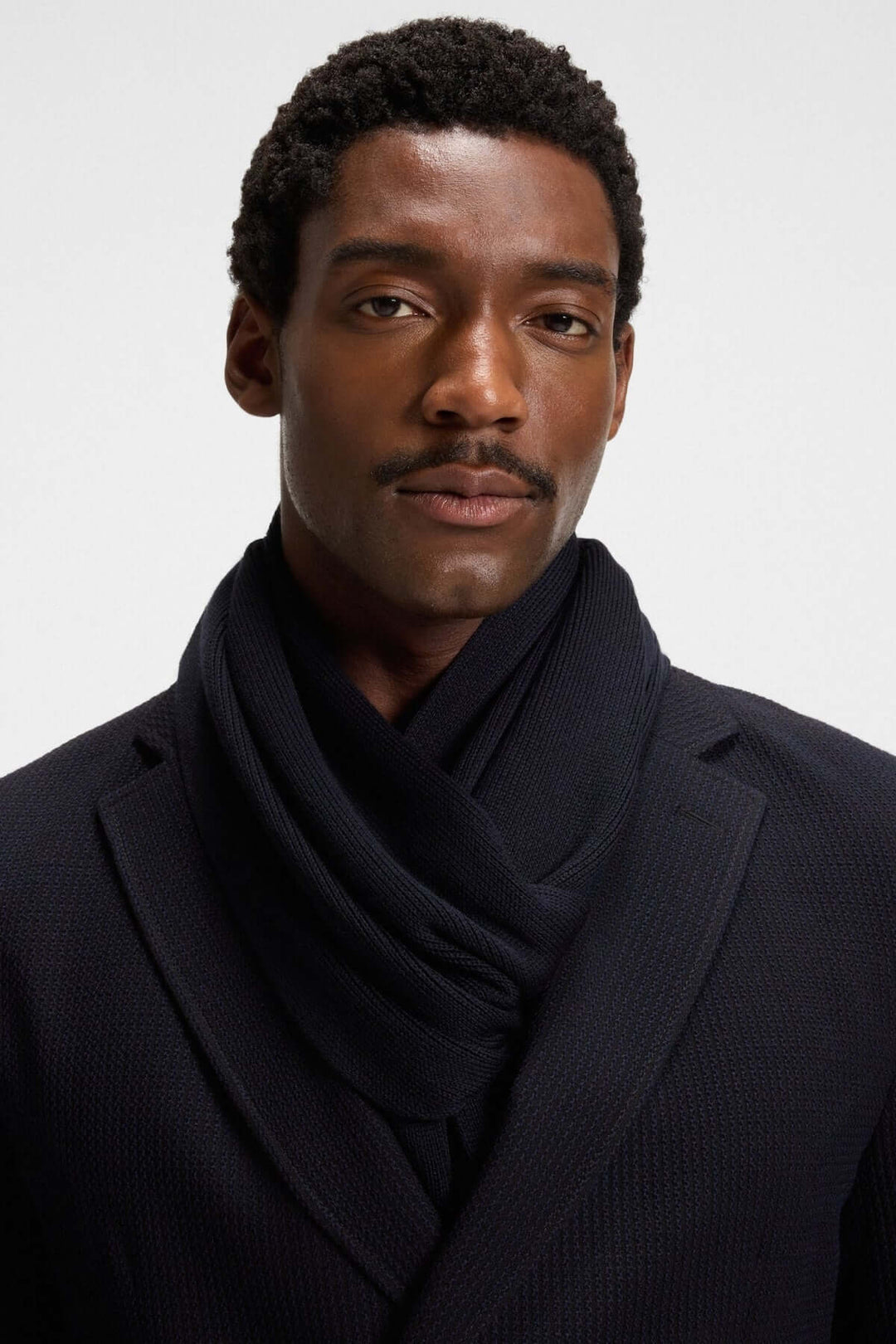 Homme portant foulard de laine vierge Boss en maille Raschel élégante, s'harmonisant avec le manteau pour un look hivernal raffiné.