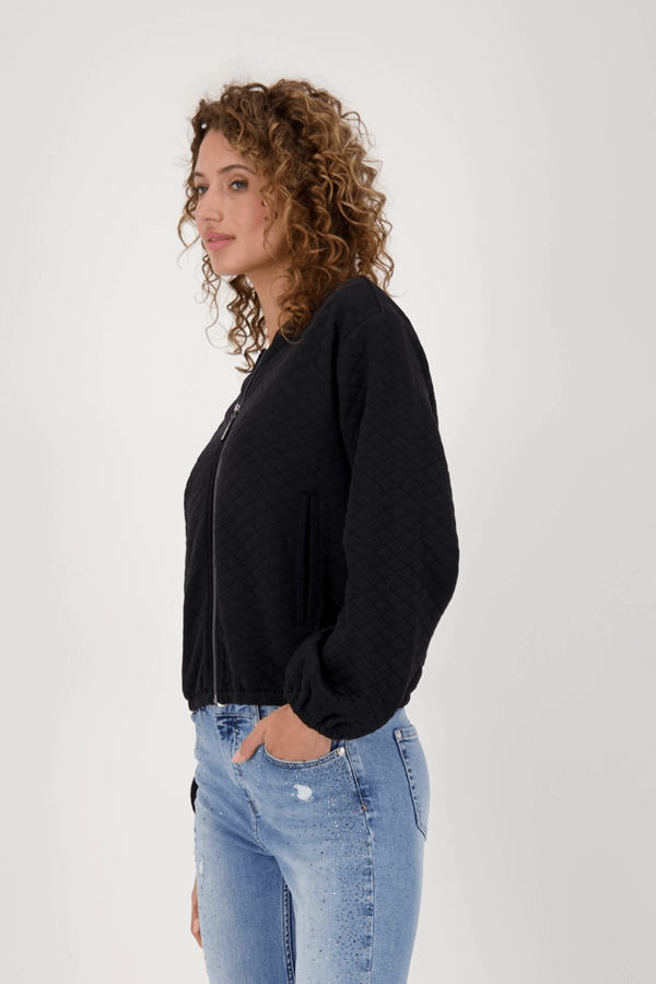Veste matelassée avec poches en tissu losanges, coupe courte et manches bouffantes, portée par une femme de profil avec jeans.
