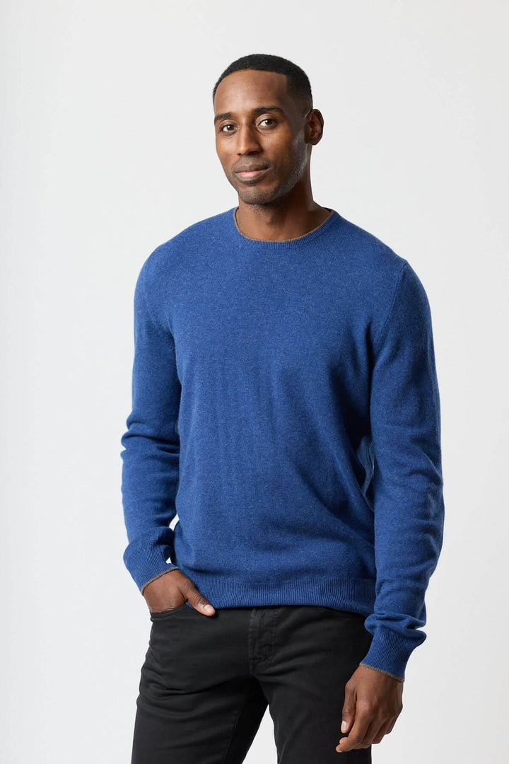 Homme portant un chandail en laine vierge et cachemire bleu, élégant et confortable, avec coudières à motif pied-de-poule.