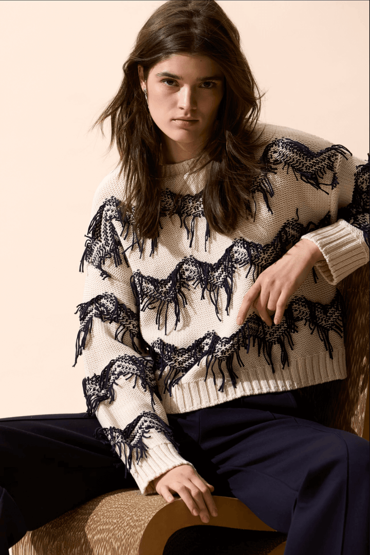 Pull tricot zigzag à franges texturées, coupe carrée et encolure sous-marine, porté avec un pantalon.