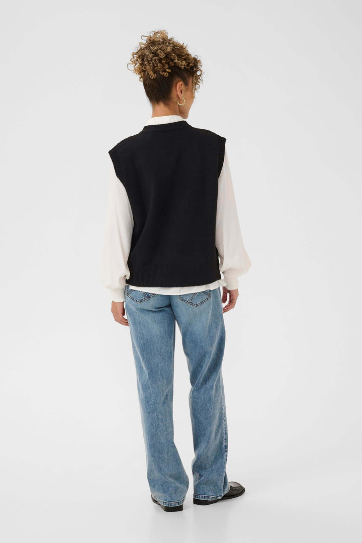 Veste Eroka sans manches en tricot à boutons dorés portée avec élégance sur une chemise blanche, vue de dos.