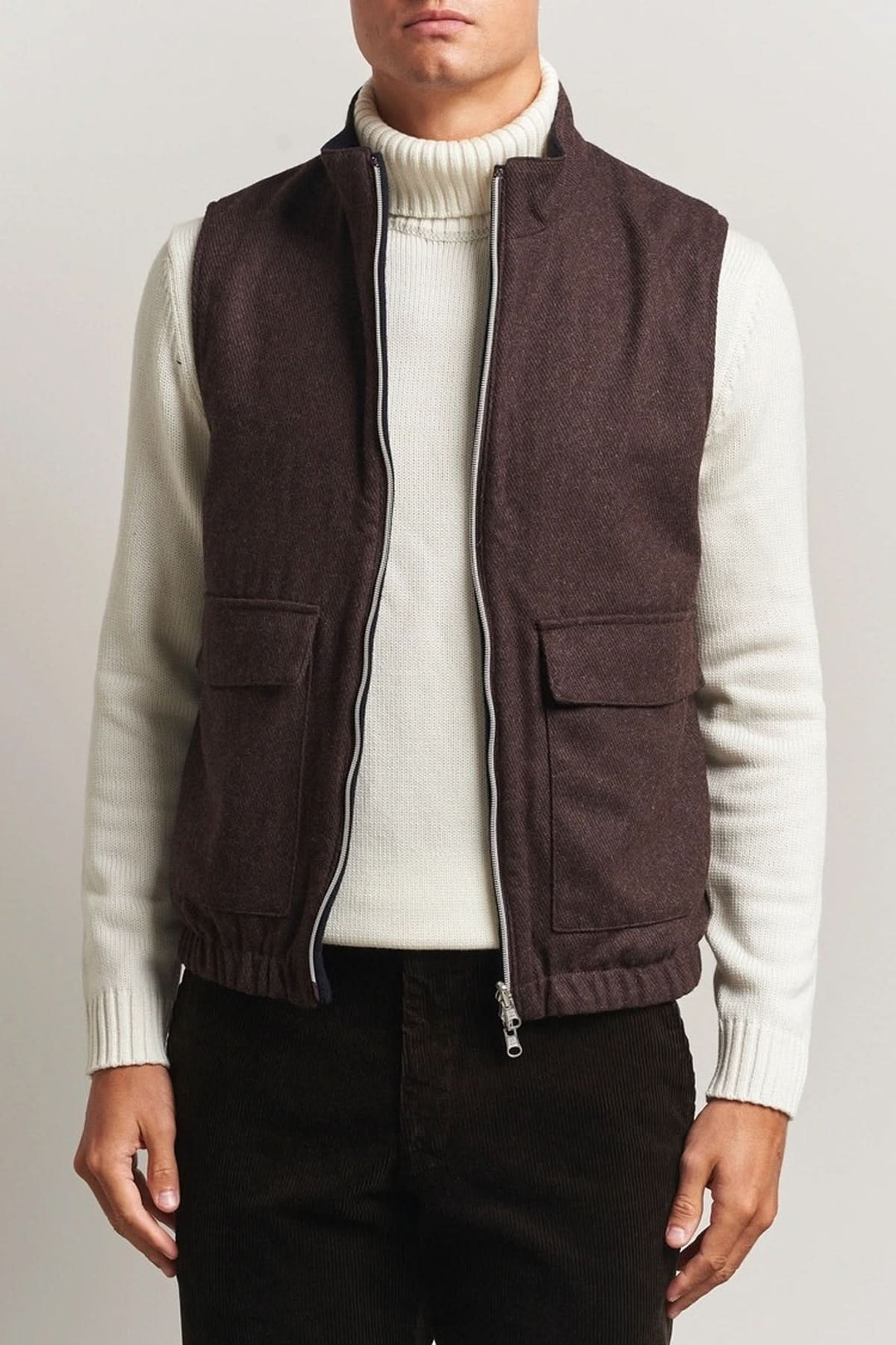 Homme portant un gilet en laine reversible marron avec col roulé blanc et fermeture à double zip.