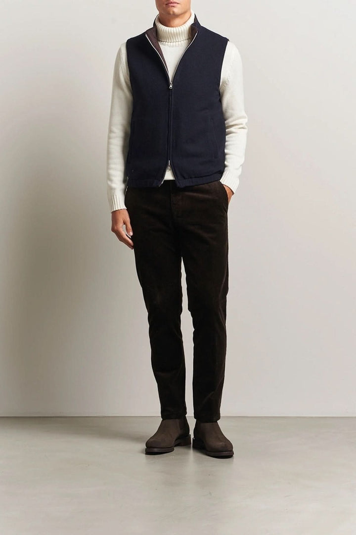 Homme portant un gilet en laine reversible avec un col roulé blanc et un pantalon noir, style élégant et raffiné.