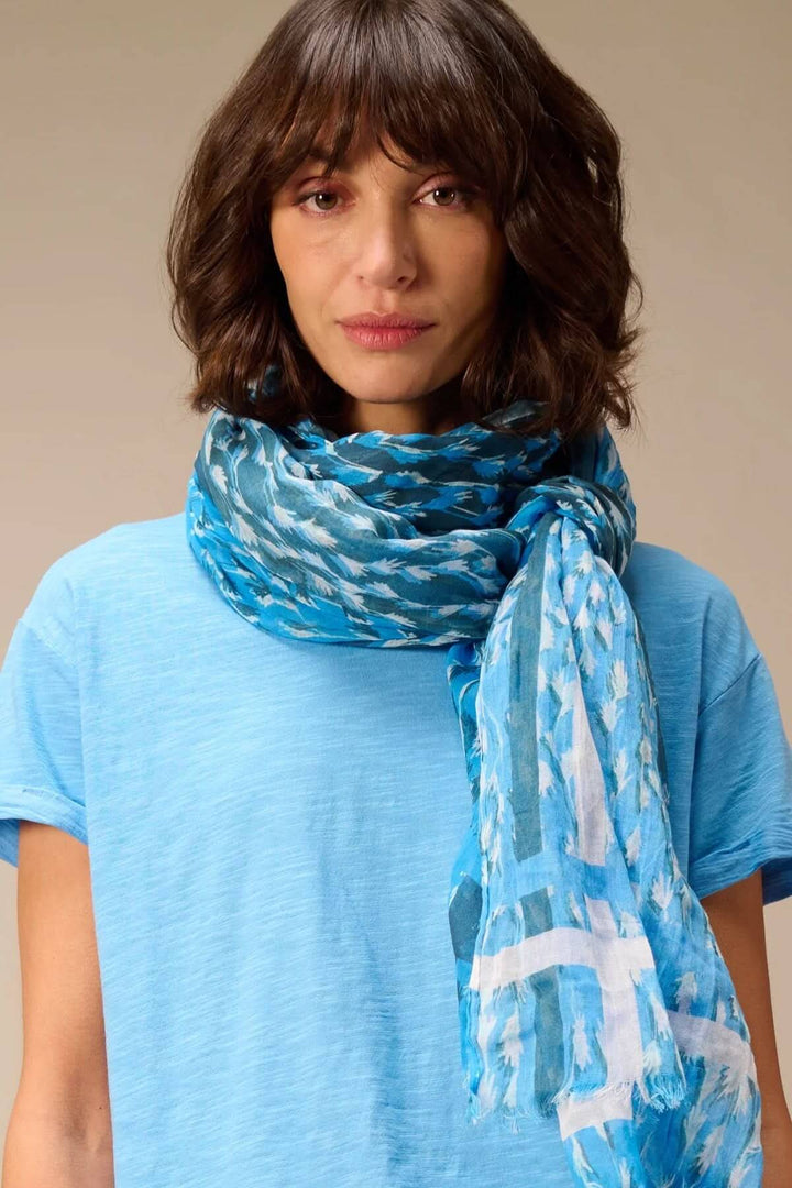 Femme portant un foulard léger à imprimé bleu avec franges délicates, accessoire polyvalent pour un look décontracté et élégant.