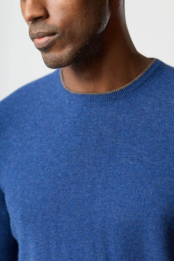 Homme portant un Chandail en laine vierge et cachemire bleu avec des coudières à motif pied-de-poule, alliant élégance et confort.