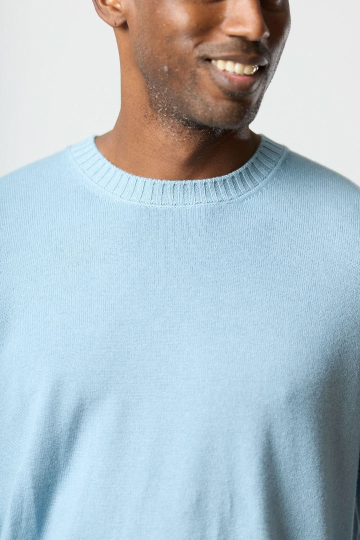 Homme portant un chandail col rond en maille douce bleu, style moderne avec ourlets côtelés.