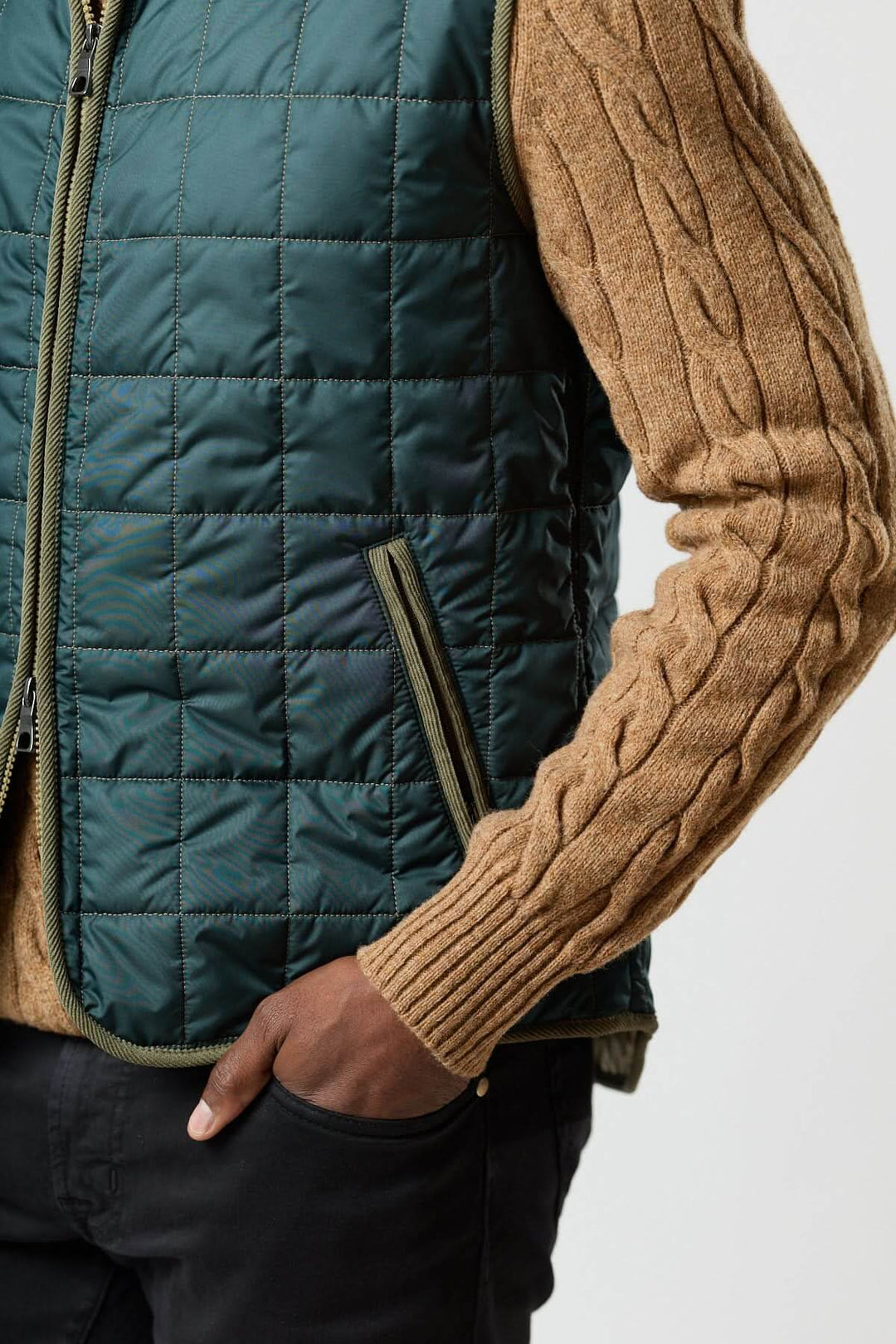 Veste sans manches matelassée avec détails en velours côtelé portée sur un pull torsadé brun ; style contemporain et élégant. 