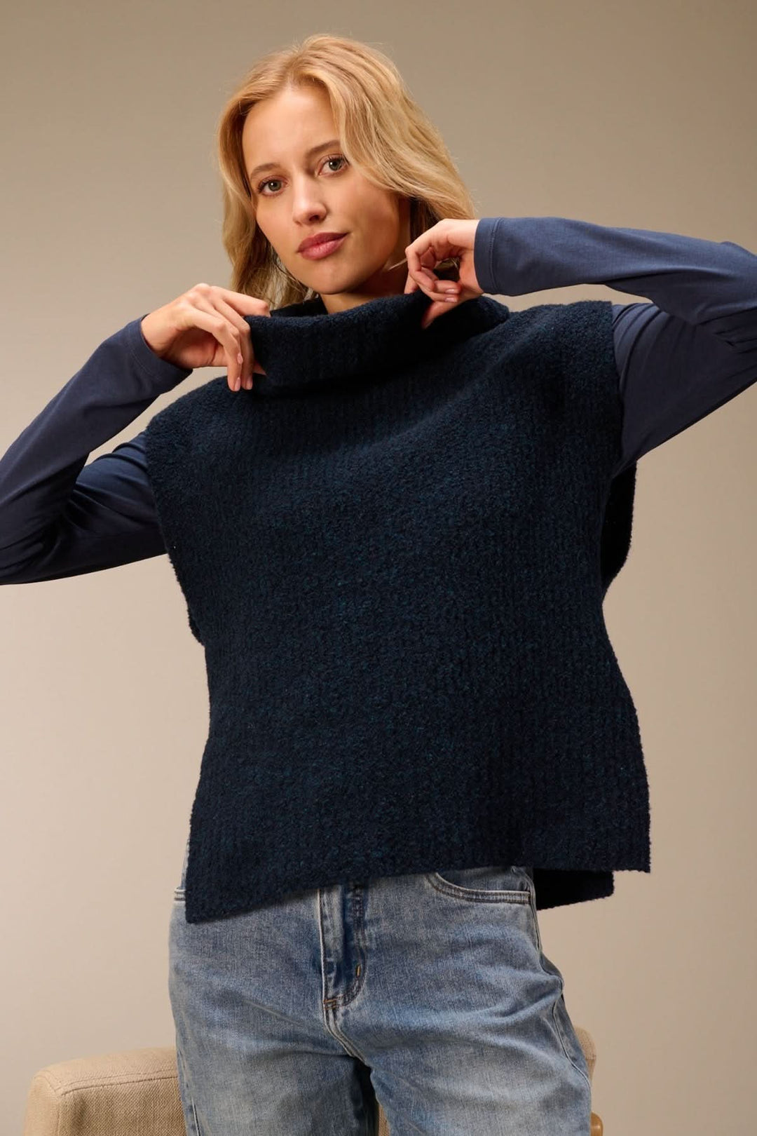 Femme portant un gilet sans manches en maille bouclée à col drapé, superposé sur un t-shirt à manches longues, style décontracté.