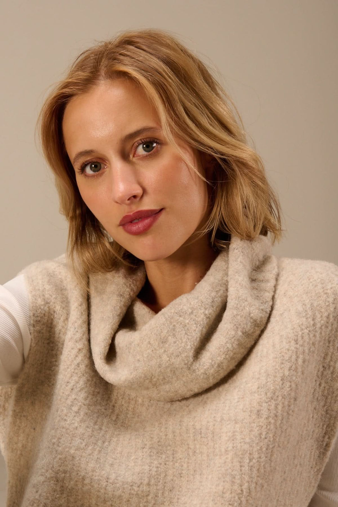 Femme portant un gilet sans manches en maille bouclée à col drapé, confortablement superposé sur un t-shirt manches longues.