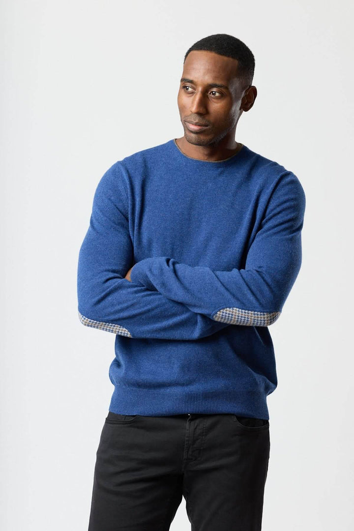 Homme portant un chandail en laine vierge et cachemire bleu avec coudières à motif pied-de-poule, style élégant et confortable.