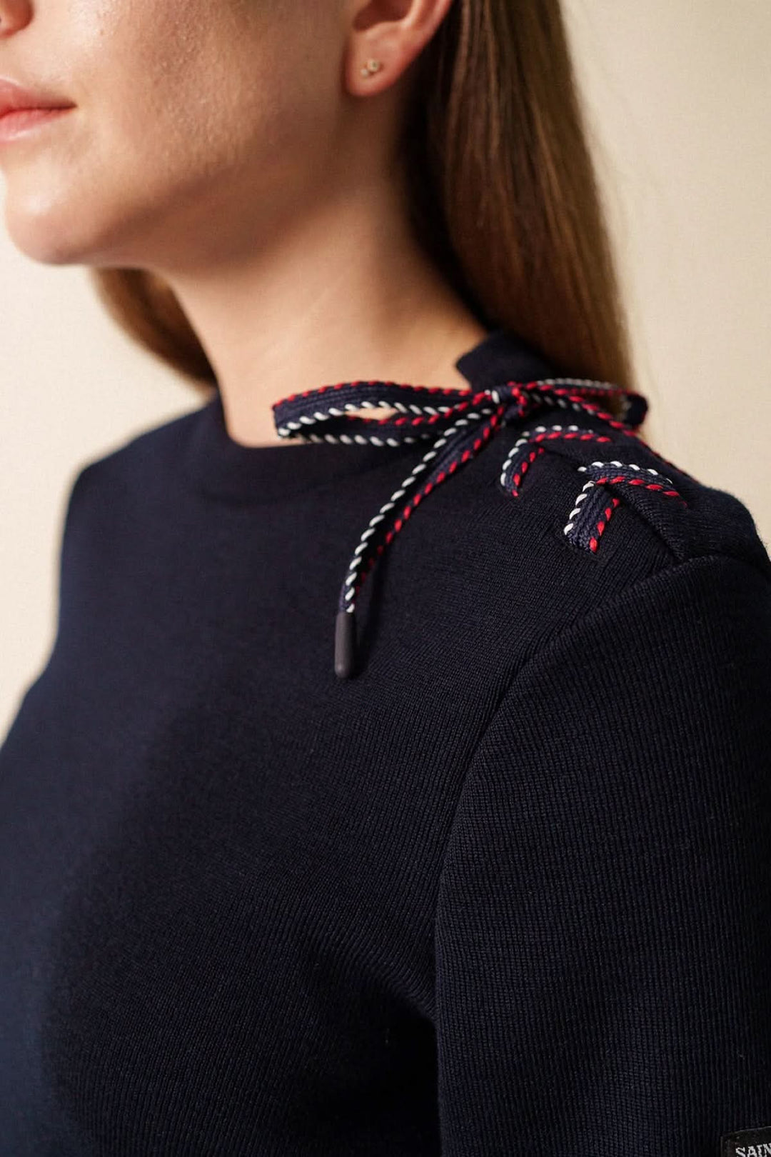 Femme portant un chandail en maille à détail nœud sur l’épaule, design féminin et raffiné avec manche longue.