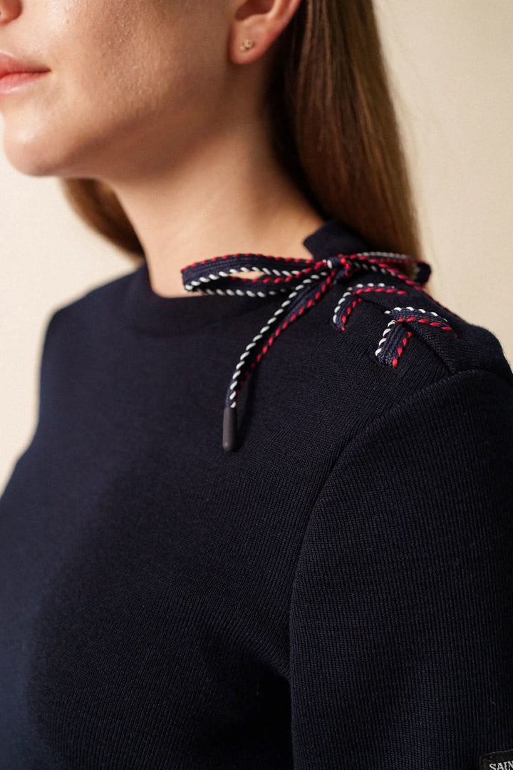 Femme portant un chandail en maille à détail nœud sur l’épaule, design féminin et raffiné avec manche longue.