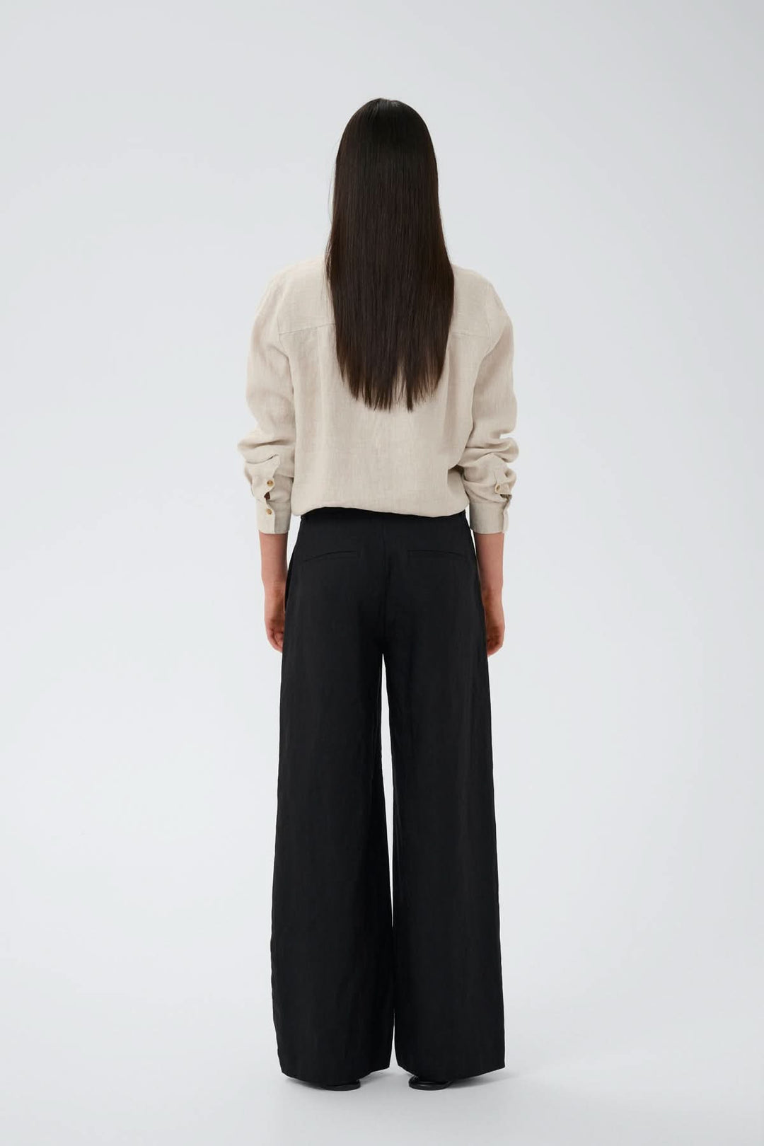 Person wearing Pantalon de lin Solina, high-waisted linen trousers with a wide-leg fit, side and back pockets, in a casual style.