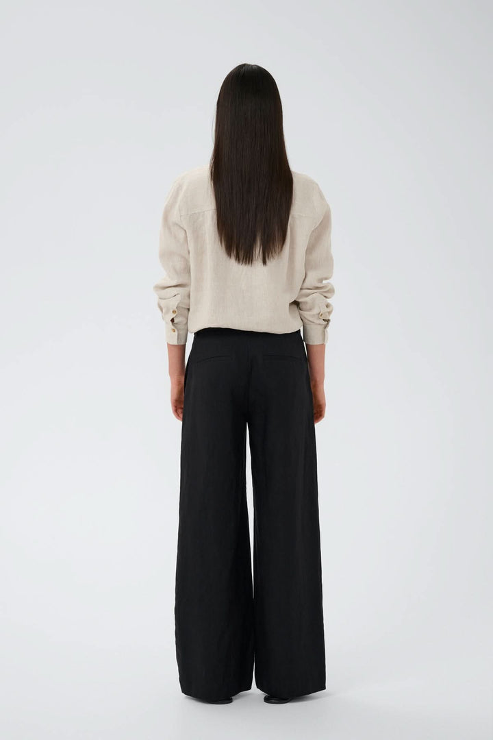Person wearing Pantalon de lin Solina, high-waisted linen trousers with a wide-leg fit, side and back pockets, in a casual style.