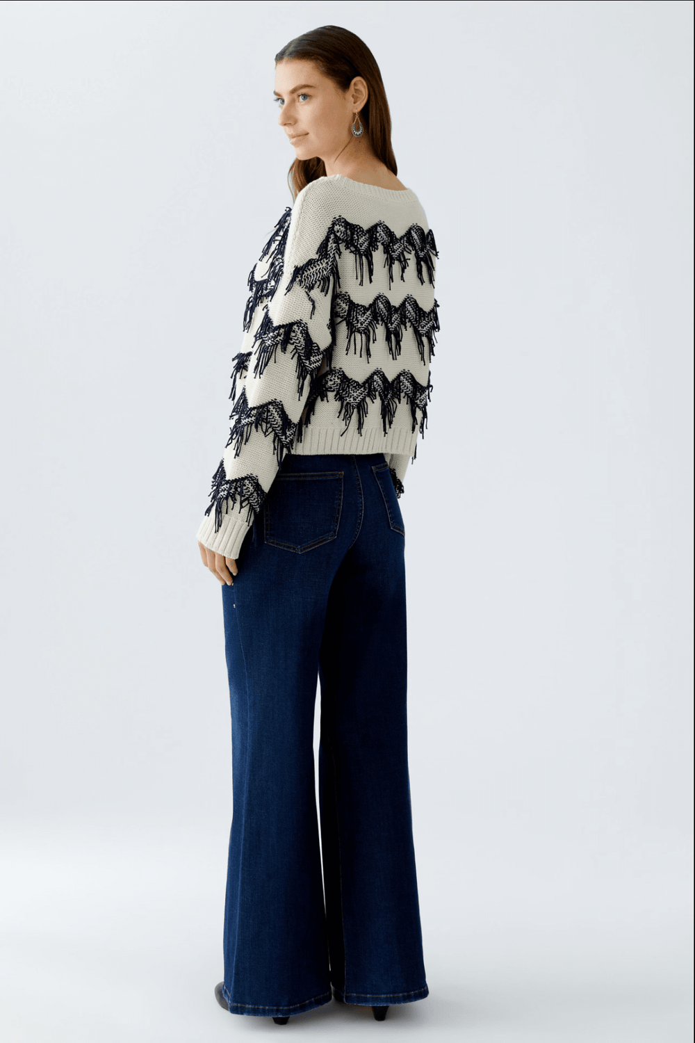 Tricot motif zigzag avec franges tricotées et coupe carrée, porté avec un jean évasé.