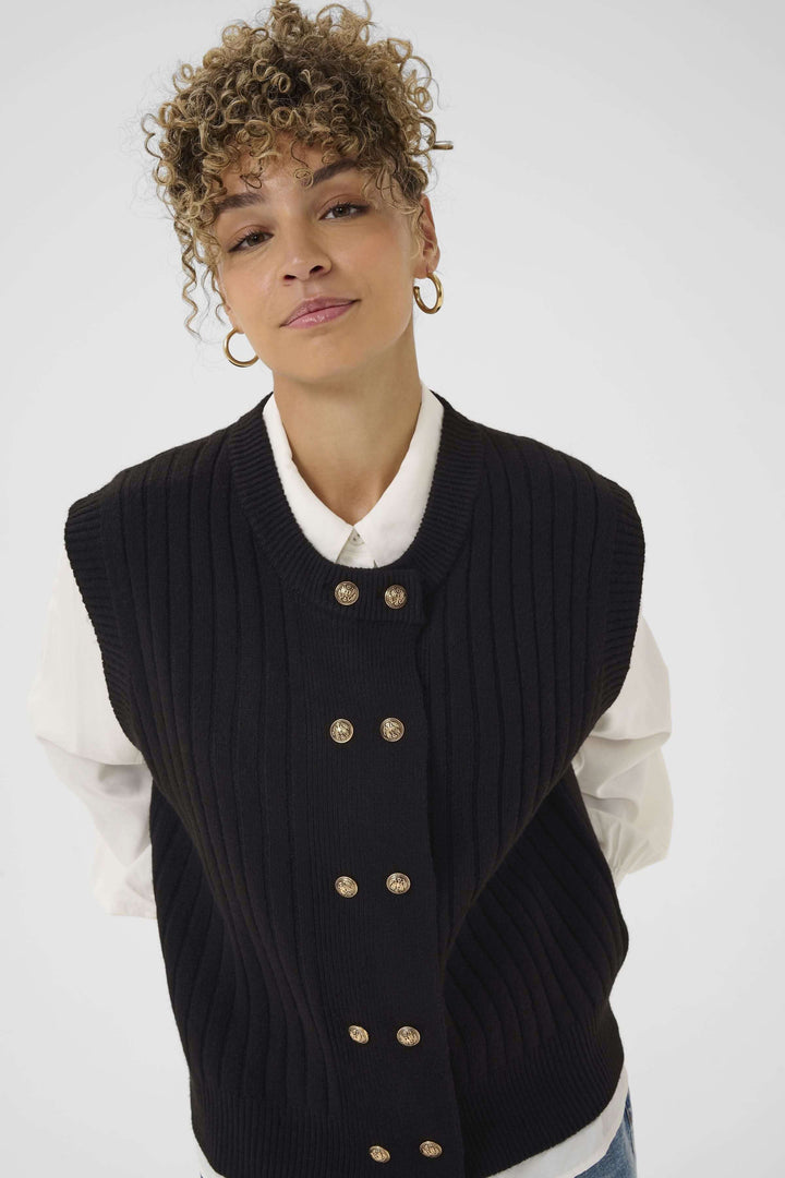 Veste Eroka sans manches en tricot à boutons dorés chic et polyvalente sur une chemise blanche, élégance décontractée.