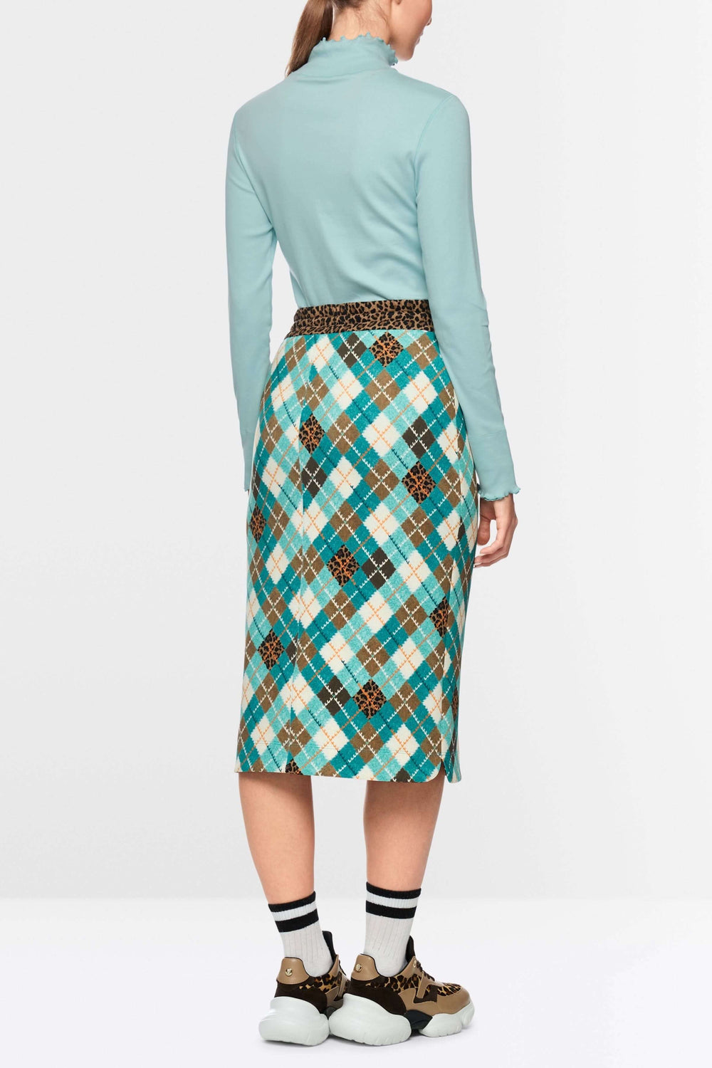 Femme portant un chandail à col montant et bordures ondulées, de dos, combiné avec une jupe à motif quadrillé multicolore.