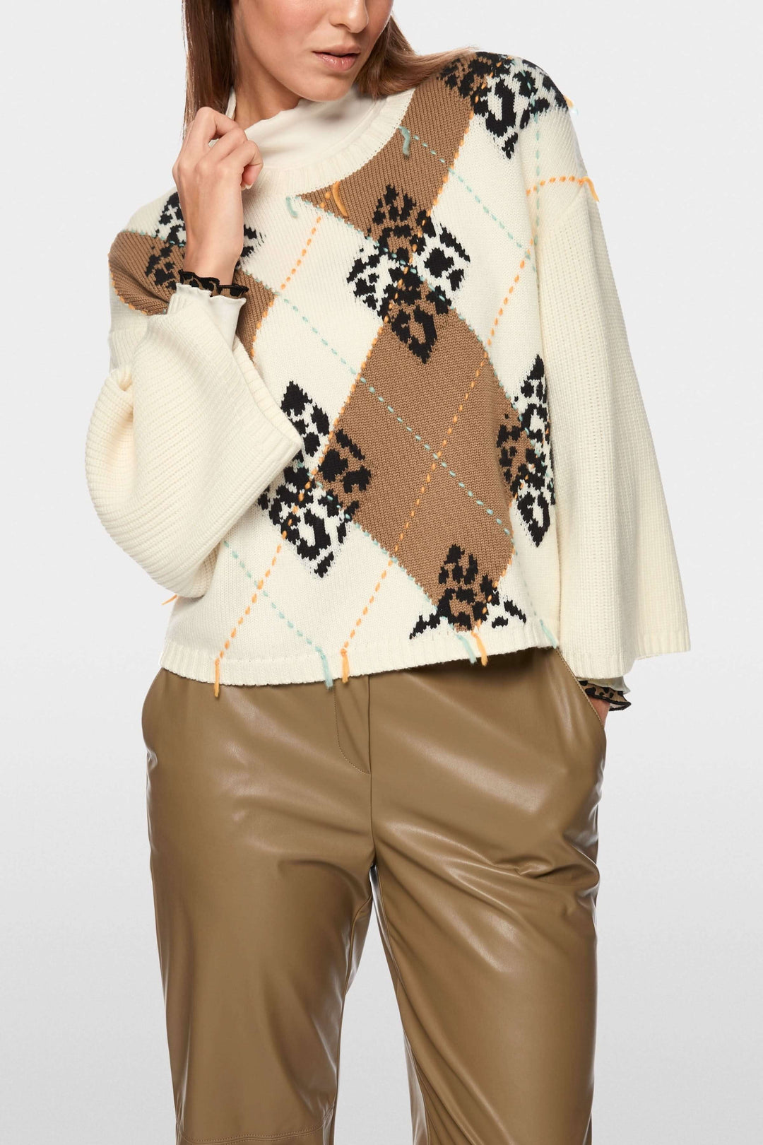 Chandail à motif losanges et accents léopard porté avec pantalon en cuir, col rond et coupe ample pour une allure moderne et confortable.