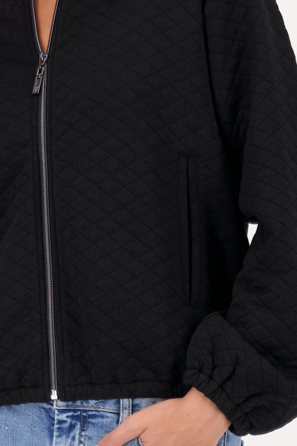 Veste matelassée avec poches noire, coupe moderne avec manches bouffantes, fermée par une fermeture éclair visible. Décris moi le produit en français.