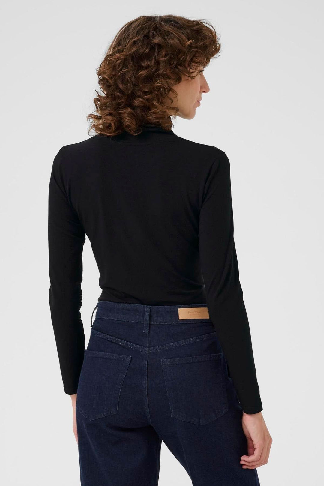 Person wearing Col roulé Efinas, a timeless black turtleneck with long sleeves and a slim fit, showcasing elegant and versatile design.