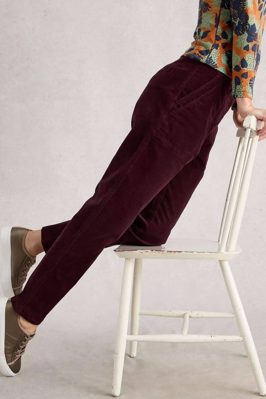 Pantalon Twister en velours côtelé prune, coupe droite fuselée, grandes poches, porté casual avec style sur une chaise vintage blanche.