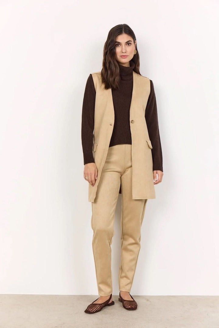 Femme en gilet sans manches beige avec pulls et pantalon assortis pour un look automnal élégant.