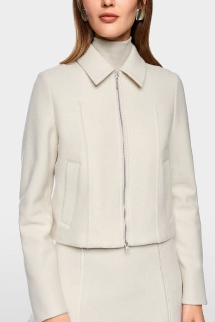 Femme portant une veste en laine vierge tendance avec fermeture éclair et poches passepoilées élégantes, look moderne, couleur crème.