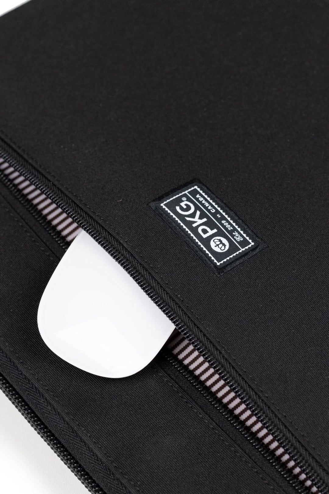 Zoom sur la fermeture éclair du sac messager PKG Wellington 10L avec logo et accessoires à l'intérieur.